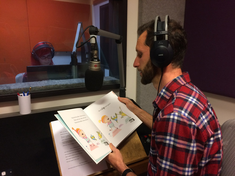 Matt smiling in front of a microphone with his picture book in hand